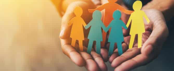 Children and adults holding a paper cutout of a family, a home, an adoption foster care program, a homeless charity, a household budget during inflation