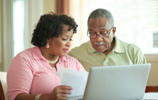 Senior couple reviewing financial documents together on a laptop, symbolizing retirement planning and budgeting.