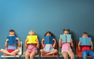Cute little children reading books while sitting near color wall