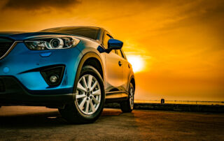 Blue compact SUV car with sport and modern design parked on concrete road by the sea at sunset. Environmentally friendly technology. Business success concept.