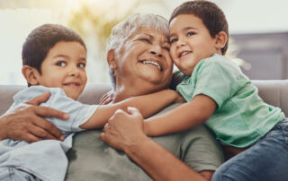 Children, hug and grandmother on a sofa, happy and smile, love and laugh while bonding on their home visit. Kids, grandchildren and boy embrace grandma on a couch, relax and hugging in a living room.