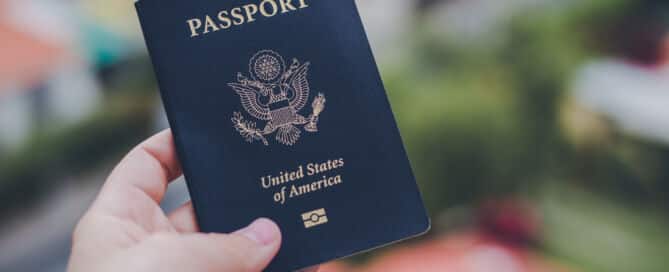 One single hand holding a blue American passport in front of a blurry background