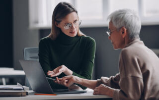 Confident financial advisor pointing laptop while discussing options with senior woman in office.